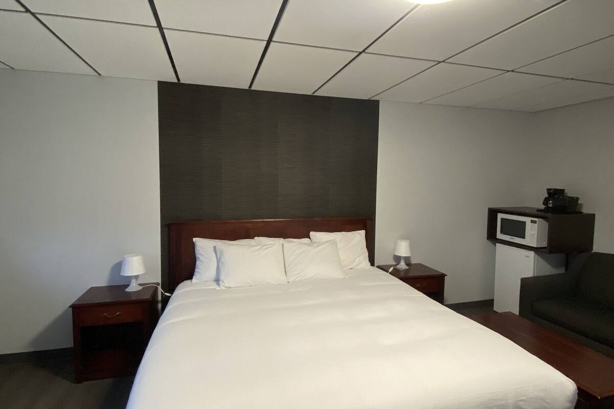 A hotel room with a large bed, two bedside tables with lamps, a microwave, and a dark-colored sofa.