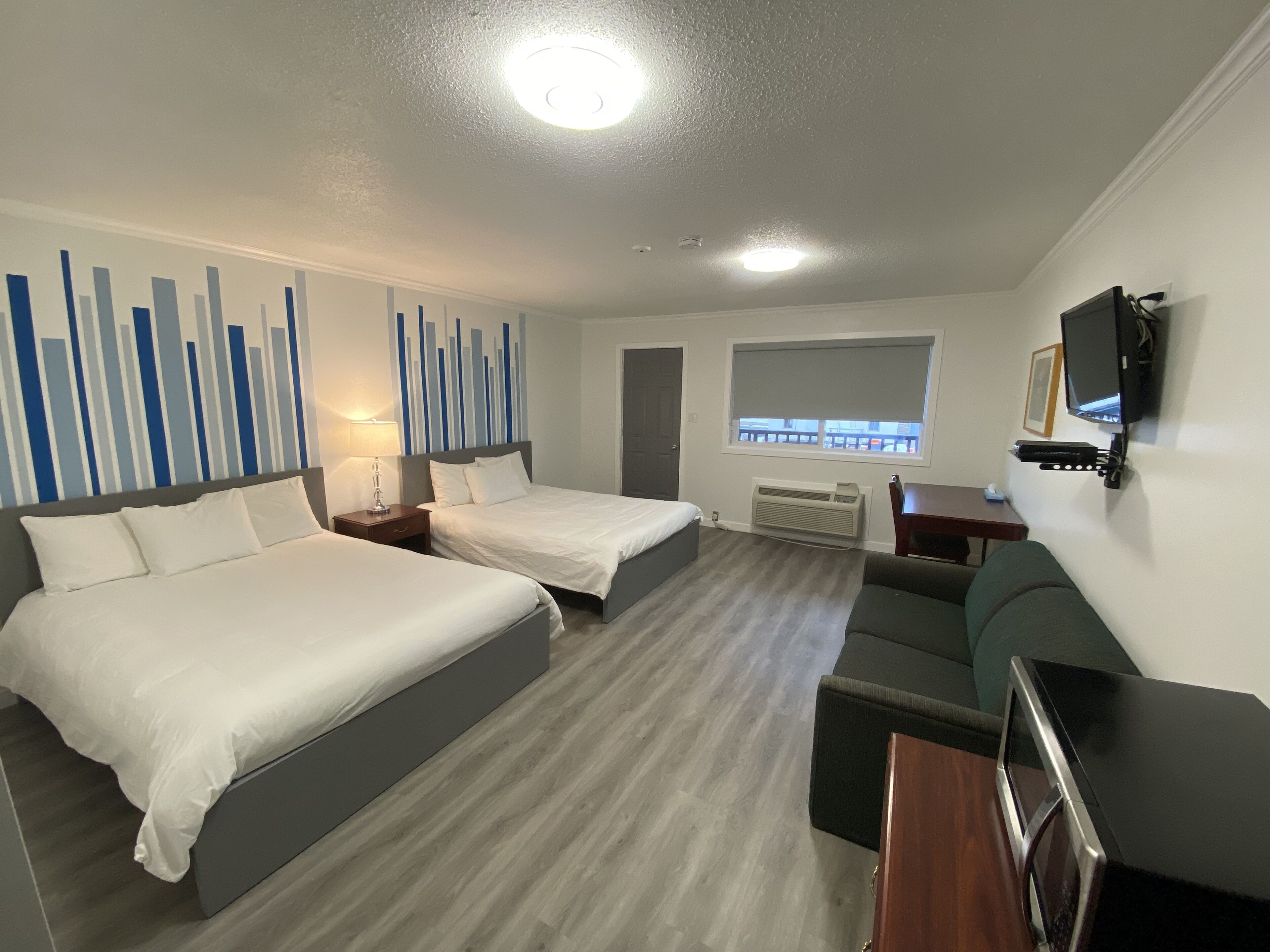 A hotel room with two beds, a TV, a desk, and a window with a view.