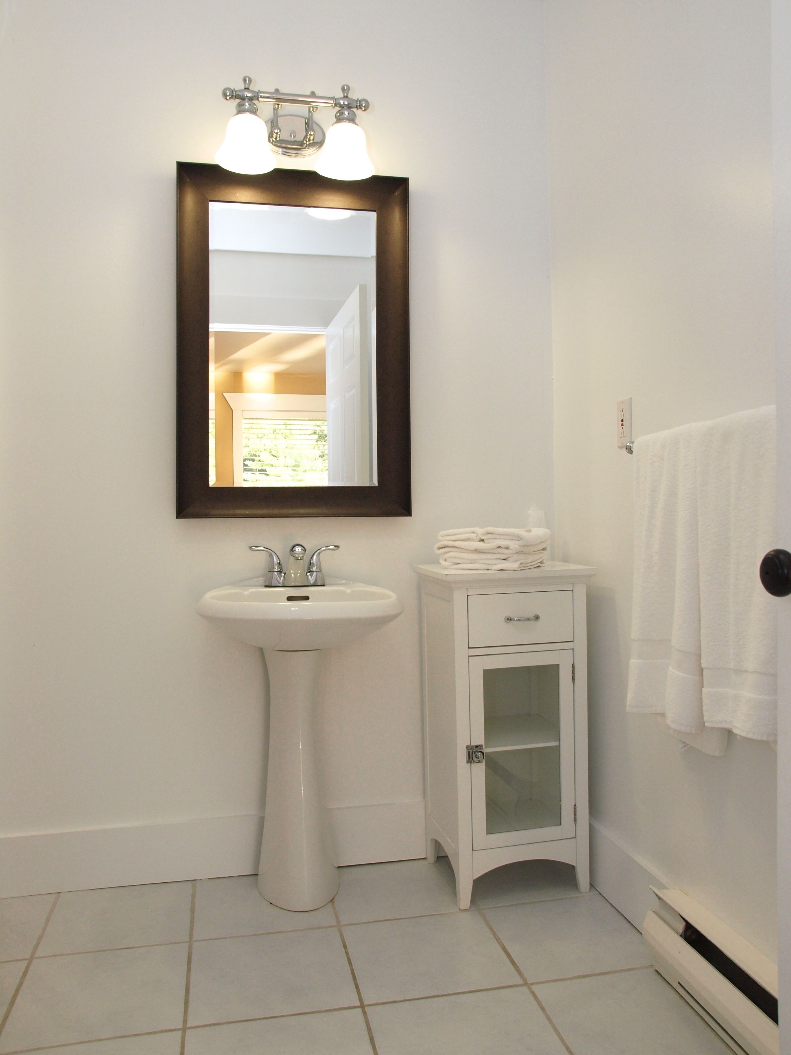 A bathroom with a pedestal sink, a mirror with lights, a cabinet, and a towel rack.