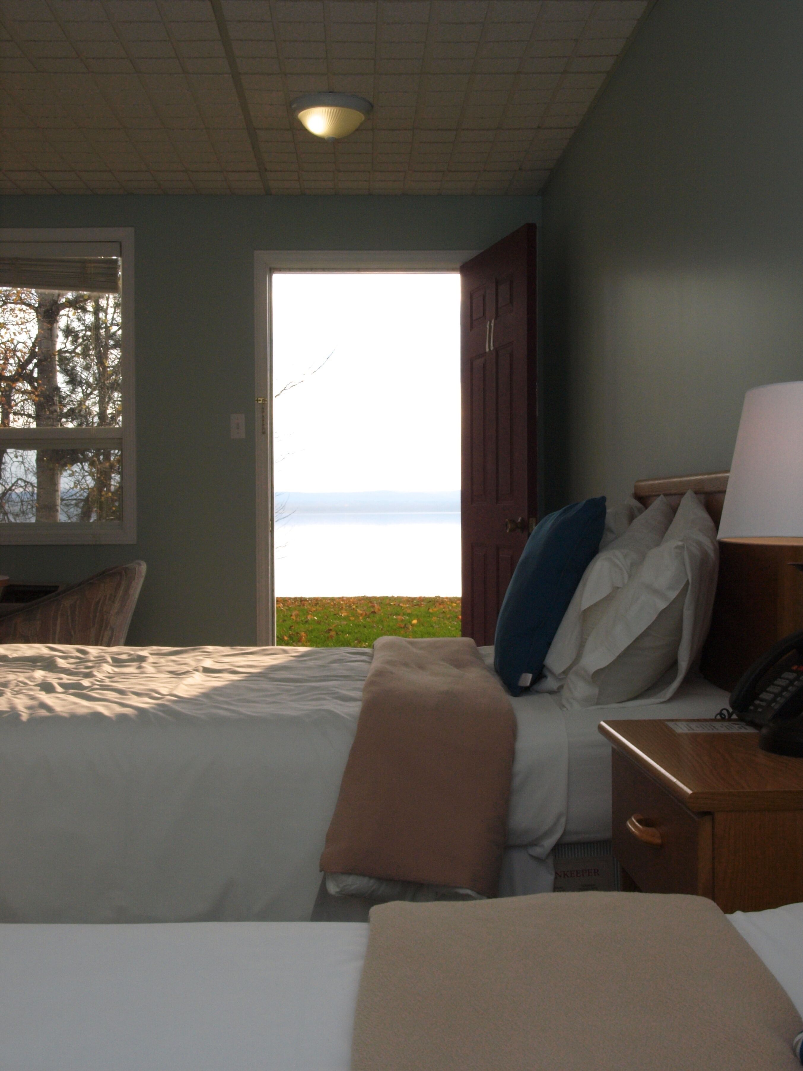 A bedroom with a bed, pillows, a bedside table with a lamp, and a window overlooking a body of water.