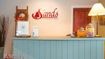 A reception desk with a sign reading "Sands on Golden Lake," a framed certificate, and two glass jars with colorful contents.