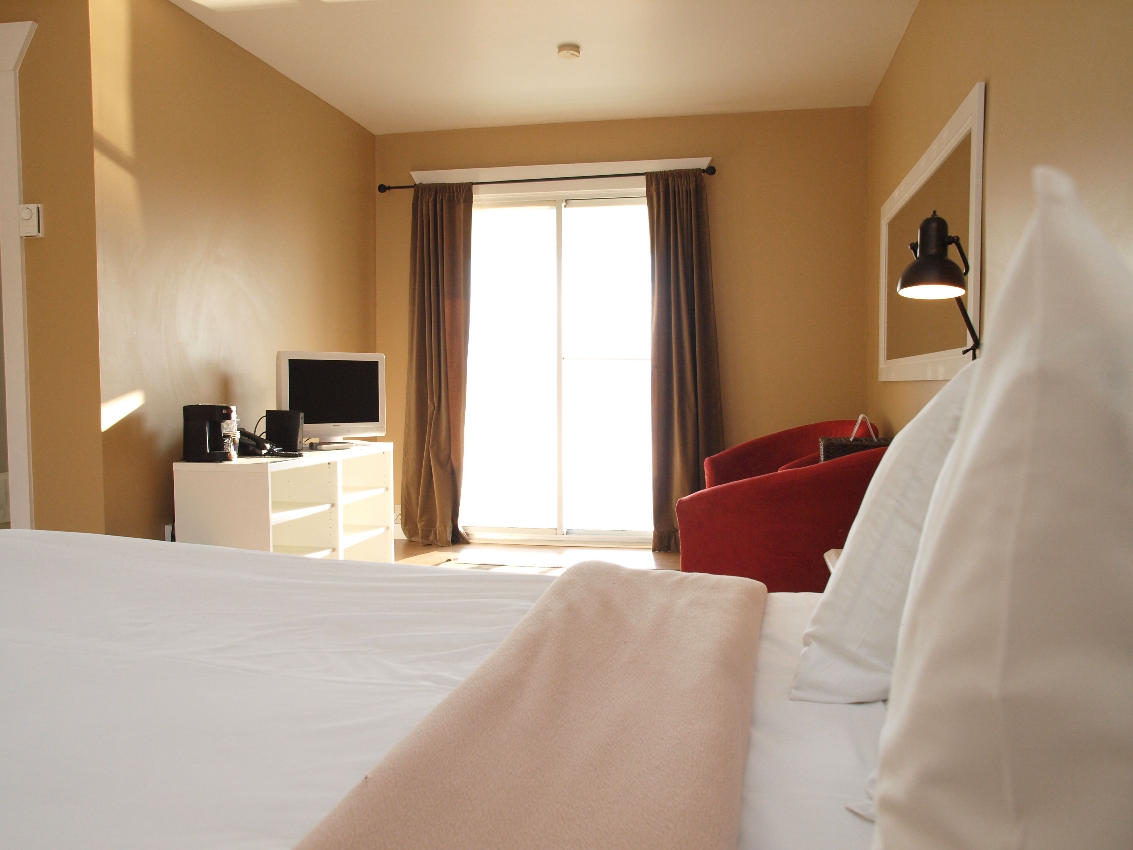 A hotel room with a bed, a desk with a computer, a red chair, and a window with curtains.