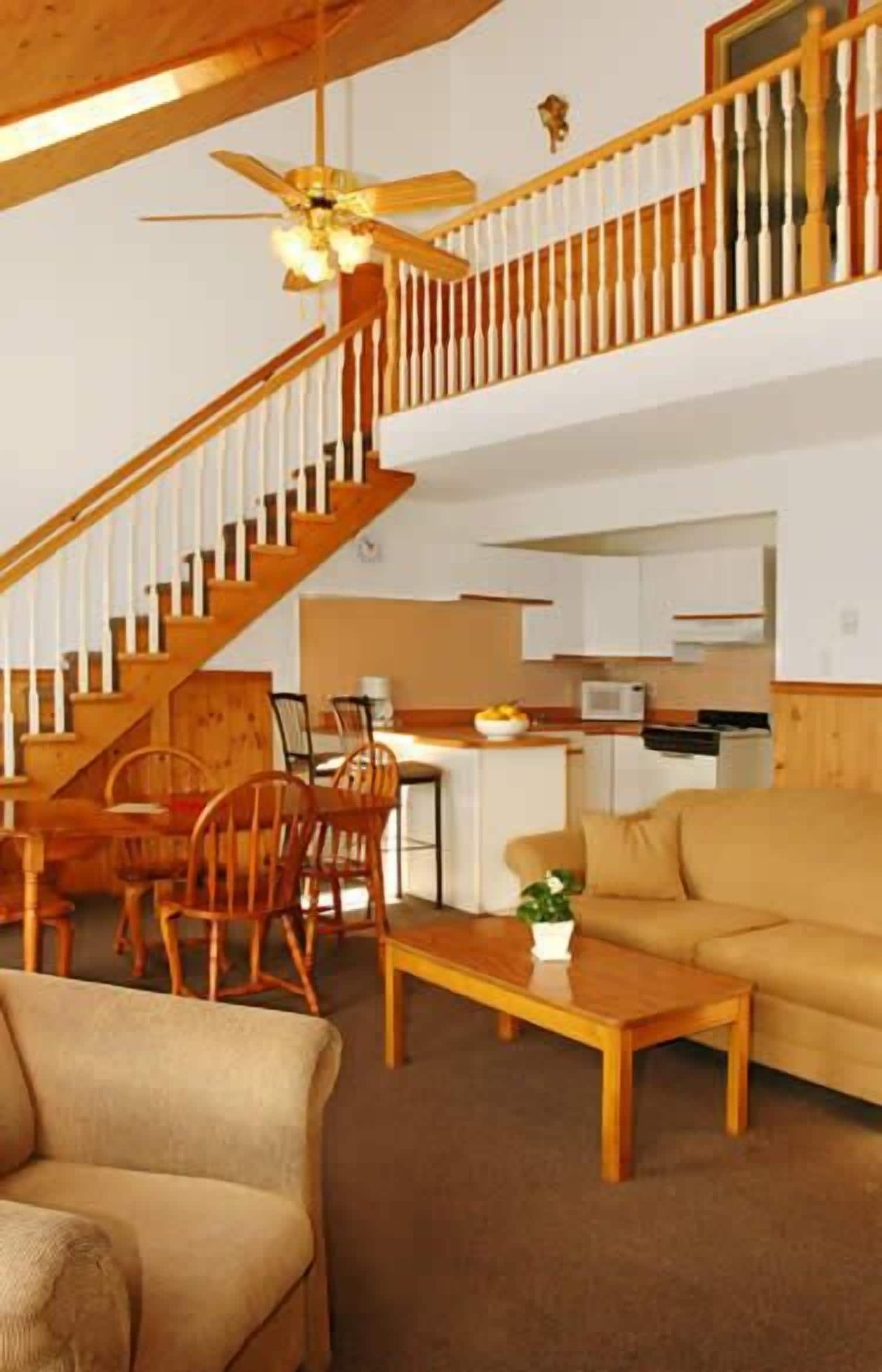 A spacious living area with a staircase, wooden furniture, and a ceiling fan.