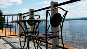Eine Holzterrasse mit Metallgeländer, zwei Stühlen und Blick auf ein Gewässer sowie entferntes Land.