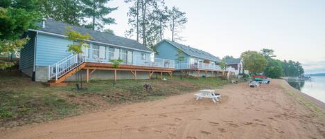 A beachfront property with multiple cabins, a sandy beach, and a lake view.