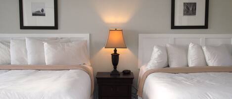 A hotel room with two beds, a nightstand with a lamp, and framed pictures on the walls.
