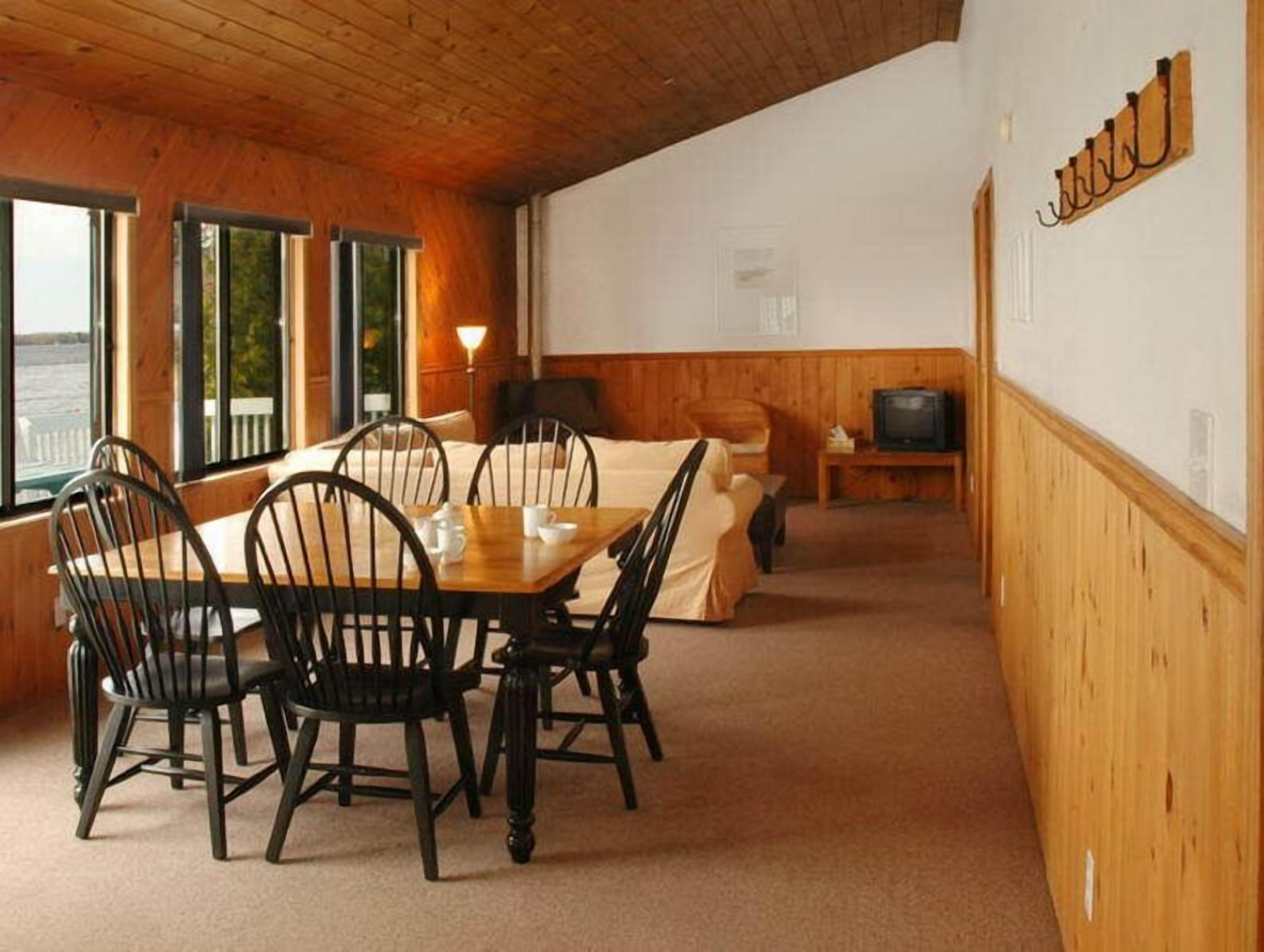 A cozy room with a wooden ceiling, a dining table with chairs, a sofa, and a television.