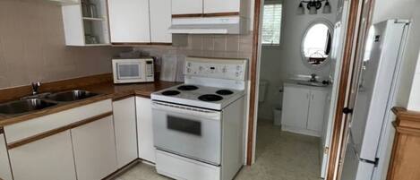 Une cuisine de taille réduite, avec des meubles blancs, une cuisinière, un four à micro-ondes et un réfrigérateur.