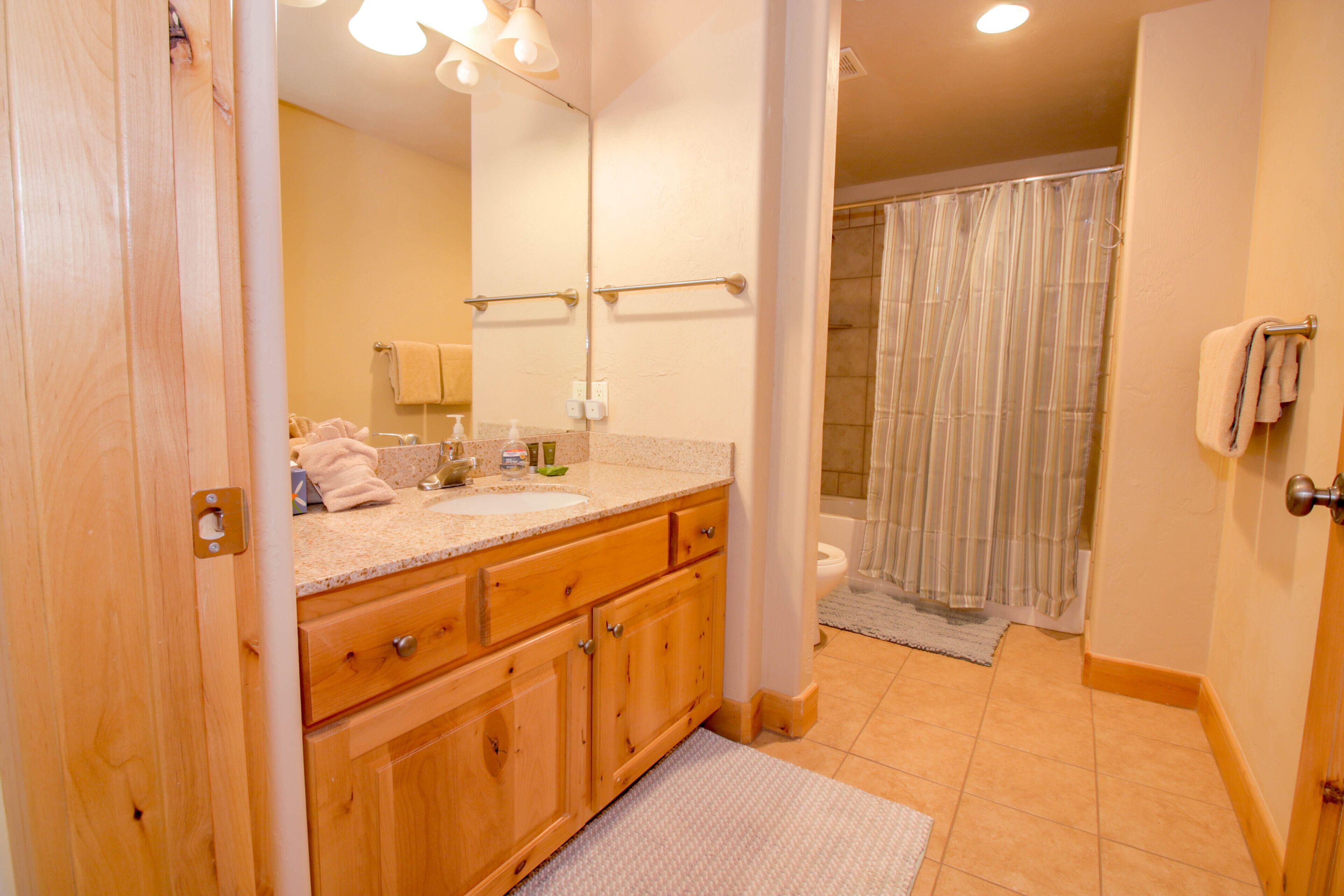 A bathroom with wooden cabinets, a sink, a mirror, and a shower area.