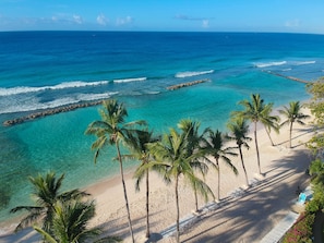 A beach with clear turquoise waters, palm trees, and a rocky breakwater.