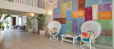 Un vestíbulo espacioso con techo alto, una araña, sillones de mimbre con cojines estampados y una pared colorida con contraventanas.