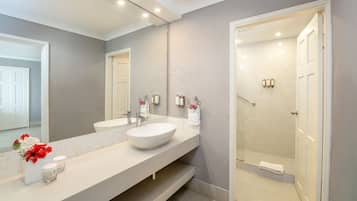A modern bathroom with a large mirror, two sinks, and a walk-in shower.