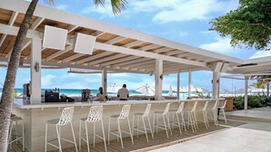 Un bar en la playa con sillas blancas y una terraza de madera.