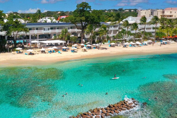 A beach resort with multiple levels of buildings, a sandy beach, and clear turquoise waters.
