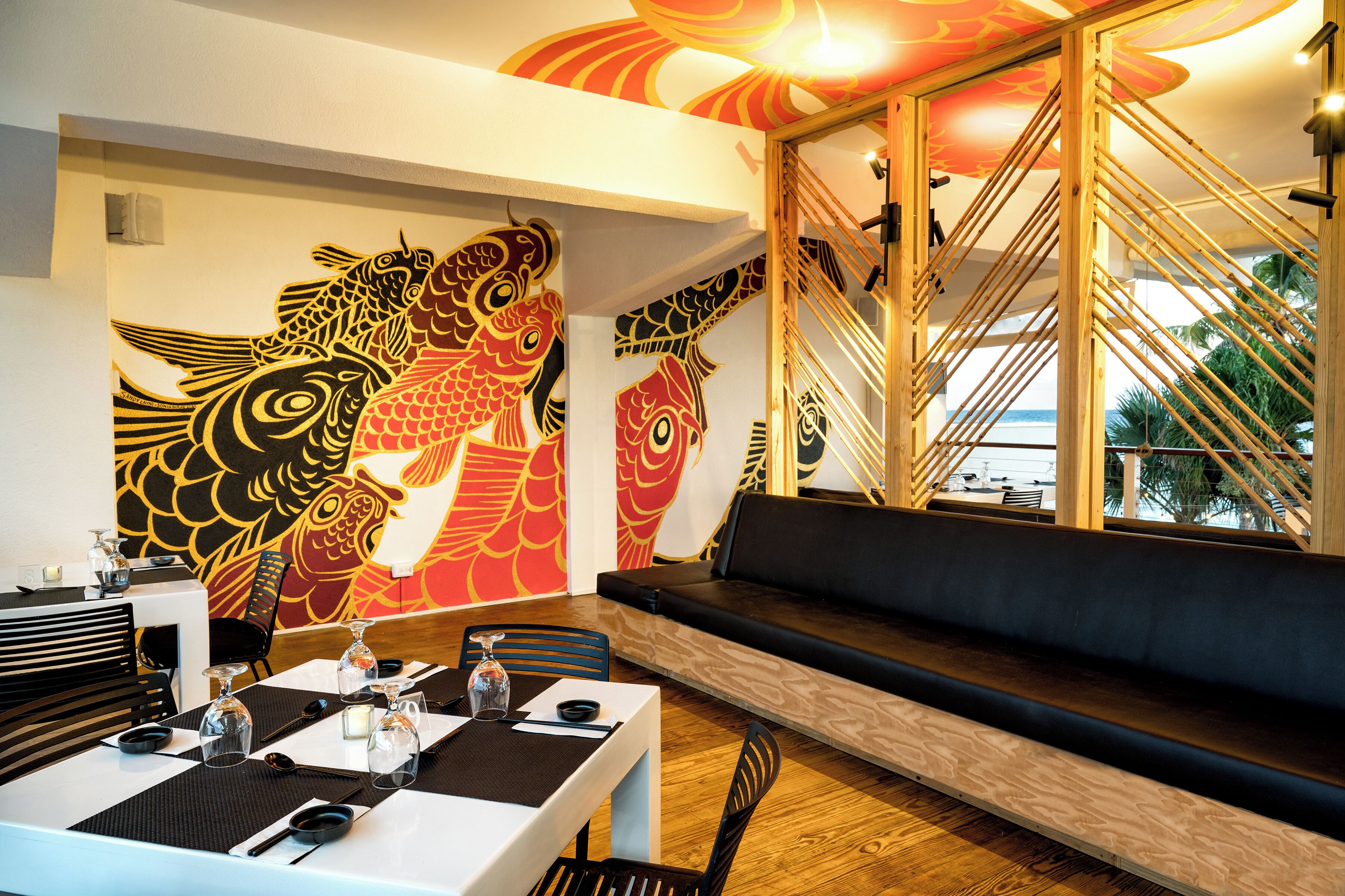 Interior de restaurante con un mural grande de peces, una escalera de madera y un área de estar con vistas.