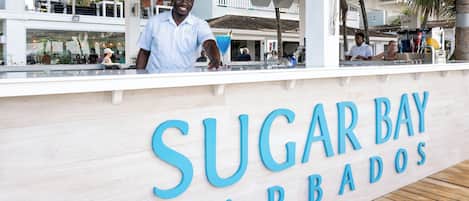 A bar named "Sugar Bay Barbados" with a wooden counter and a view of the outdoor seating area.