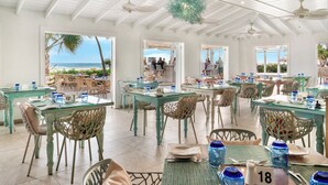 Un comedor amplio con mesas de vidrio y sillas de mimbre, con vista a una playa.
