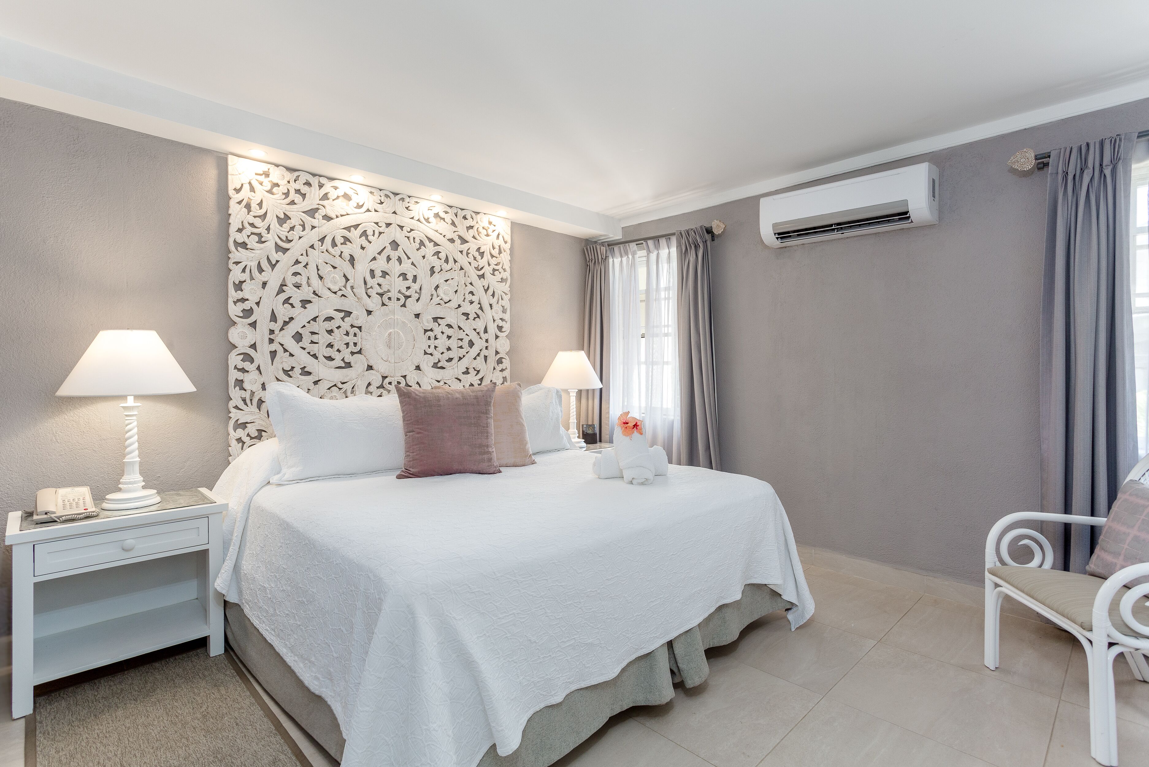 Una camera da letto ordinata con un letto, comodini, una sedia e un condizionatore.