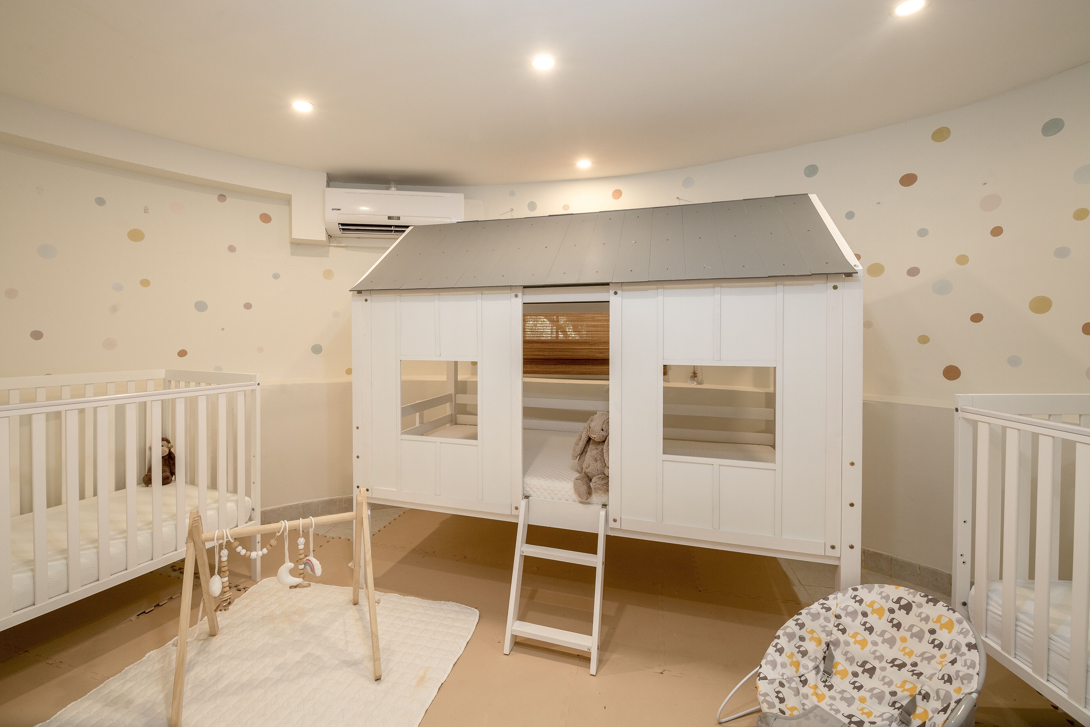 A baby room with two cribs, a playpen, and a white crib with a ladder.