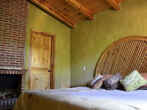 Quarto com cama de madeira, lareira de tijolos e porta de madeira.