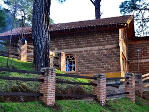 Un bâtiment en briques surmonté d’un toit en tuiles, avec une clôture en bois et une petite fenêtre en arc de cercle.