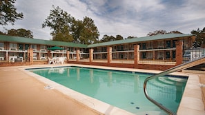 A pool area with a brick building, outdoor seating, and a covered patio.