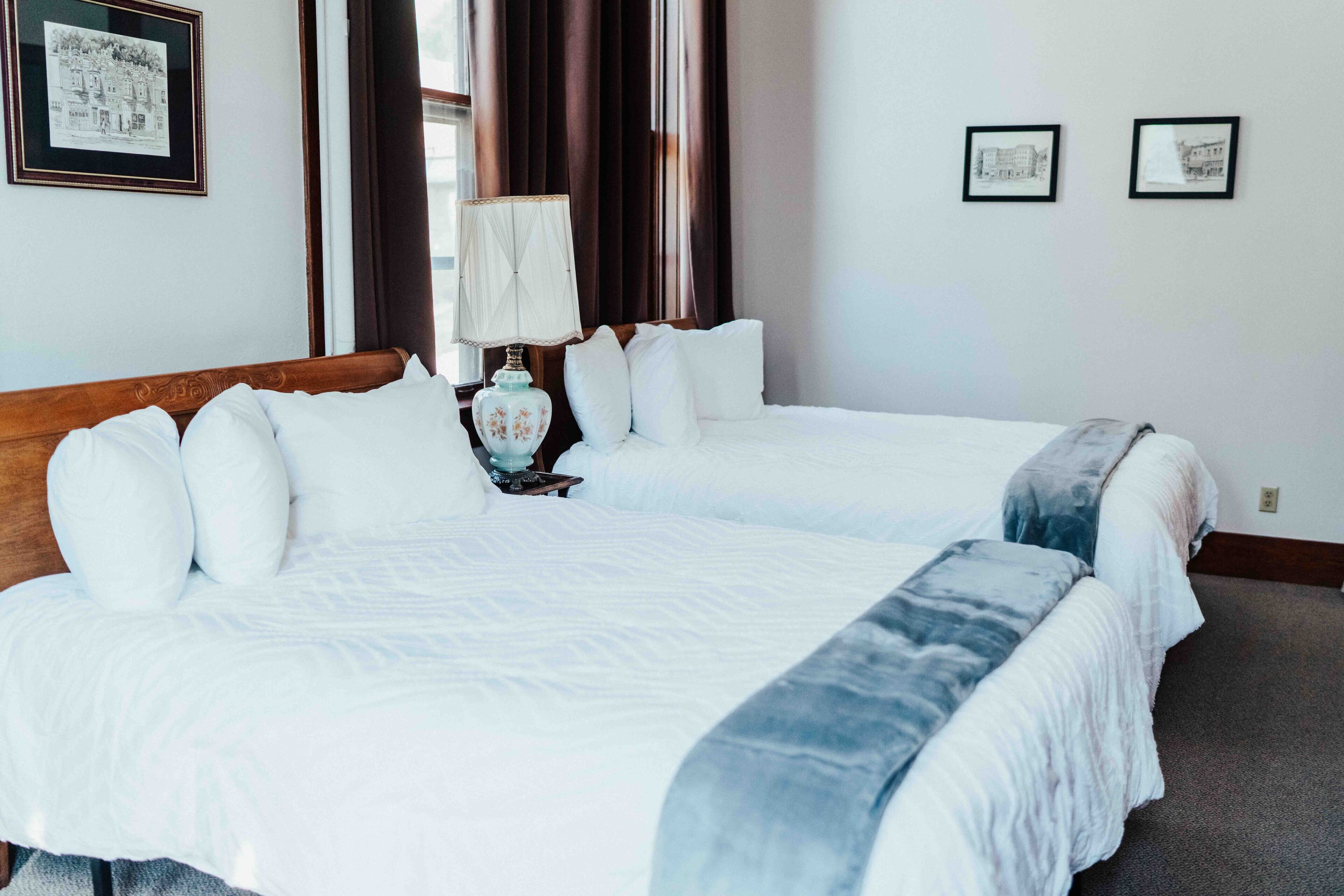 A hotel room with two beds, a nightstand with a lamp, and framed pictures on the walls.