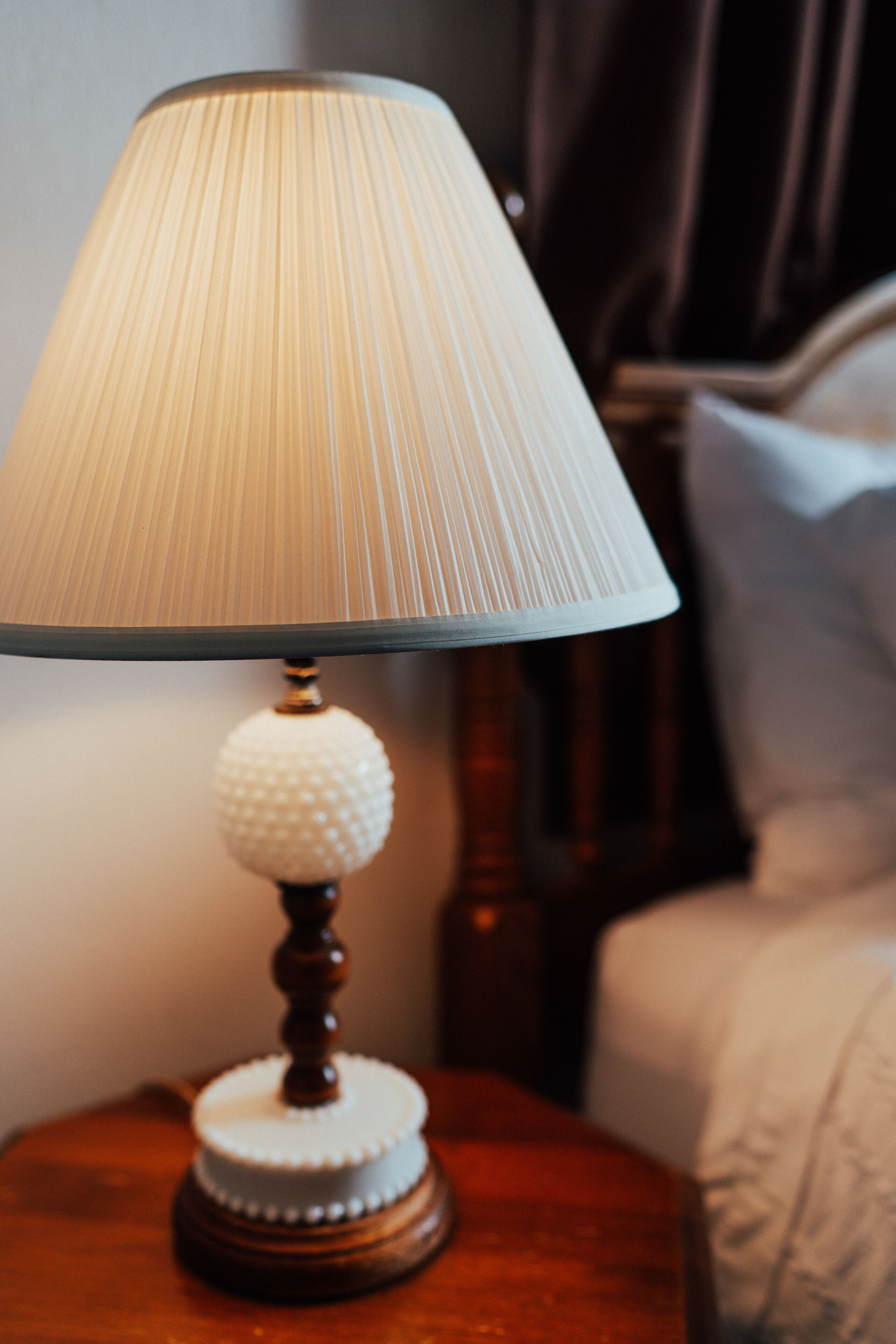 A bedside table with a lamp, a wooden nightstand, and a bed with a headboard.