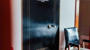 A black safe with the inscription "City of Lead - Engineer" and "Herring Hall-Marville Safe Co." in a room with a patterned carpet and a wooden chair. - Town Hall Inn (Lead)