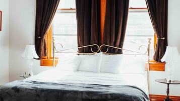 A hotel room with a bed, curtains, a lamp, and a view of the outdoors.