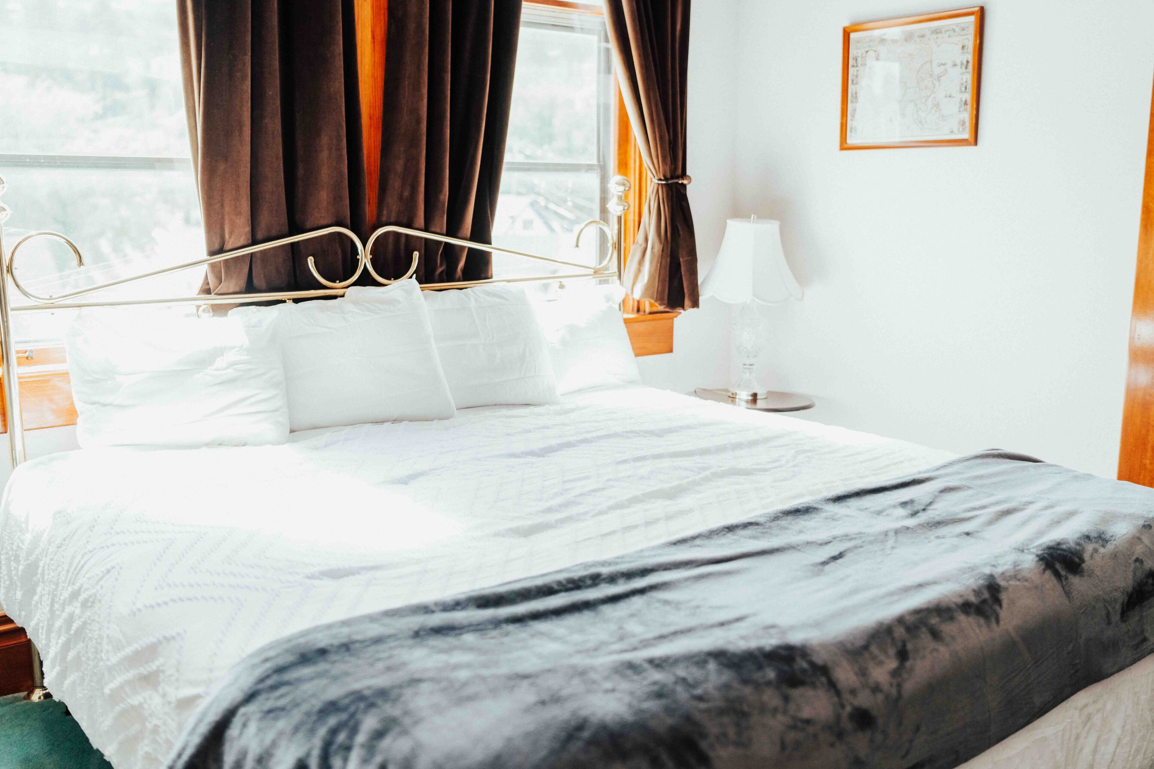 A neatly made bed with white linens and a dark patterned throw blanket.