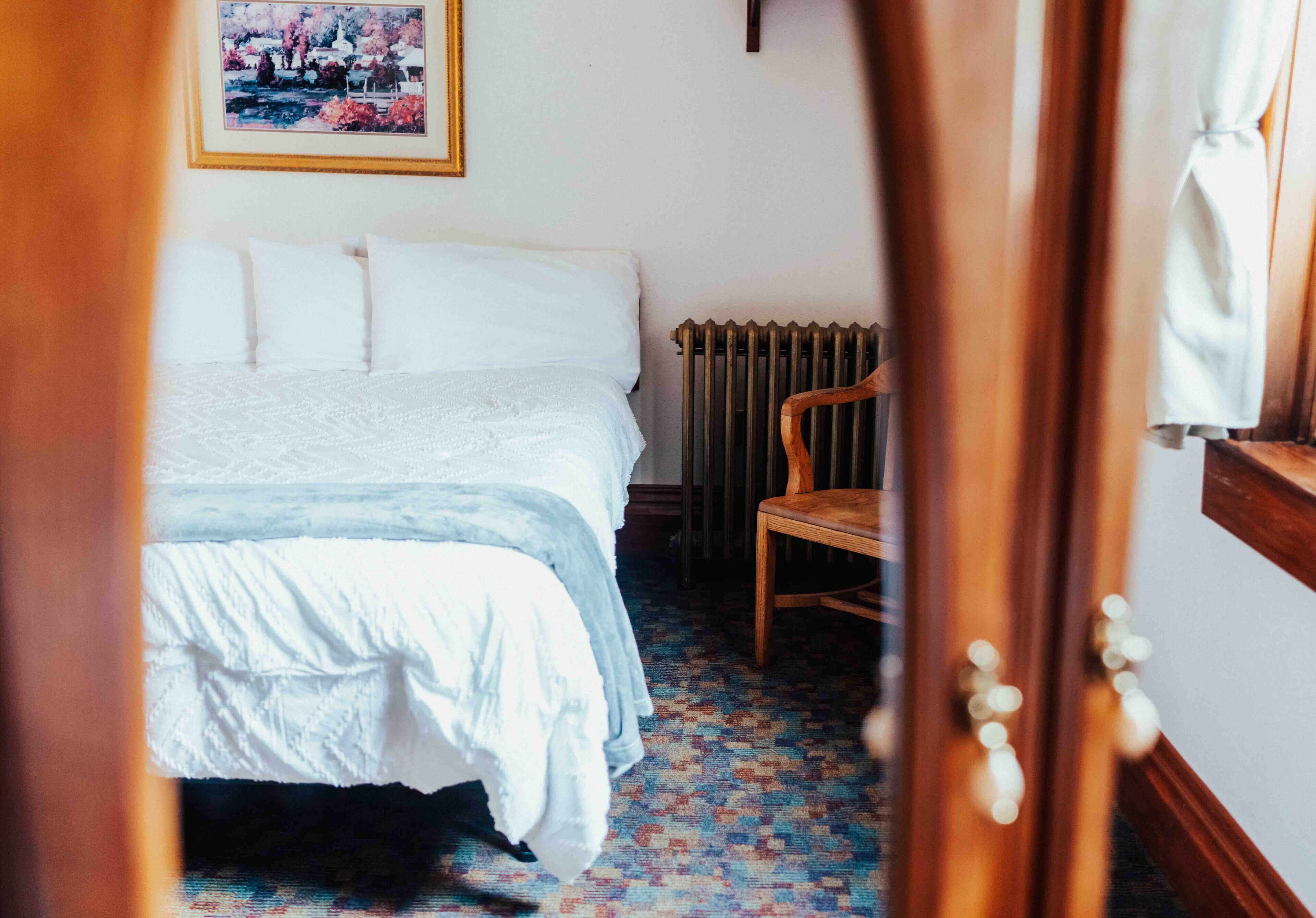 A bedroom with a bed, a radiator, a chair, and a door.