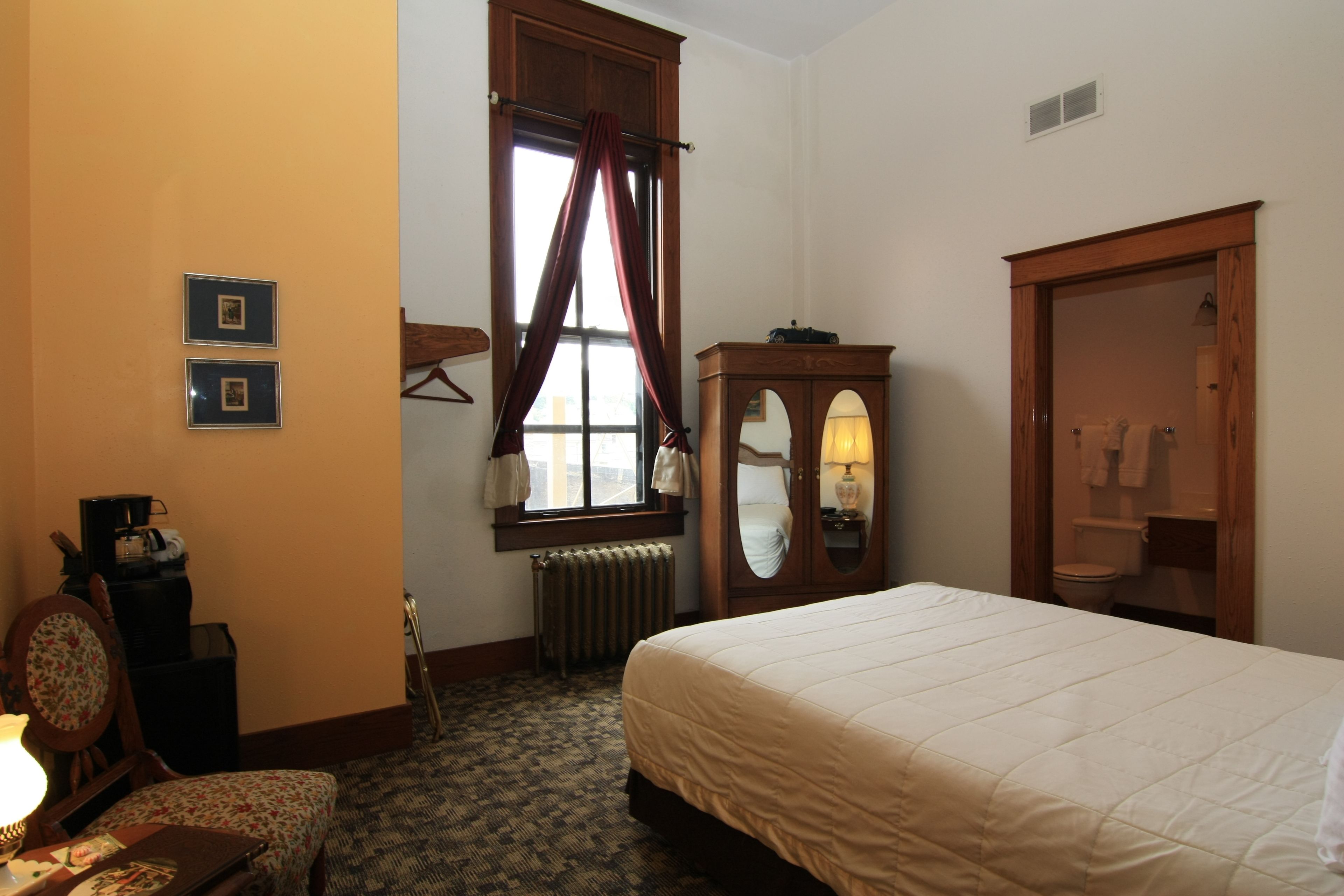 A hotel room with a bed, a dresser, a mirror, a radiator, and a window with curtains.