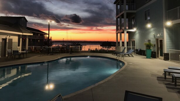A swimming pool with lounge chairs and a view of a sunset over water. - Anchor Inn (Chincoteague)