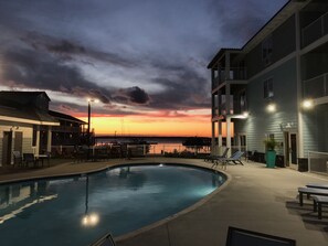 A swimming pool with lounge chairs and a view of a sunset over water.