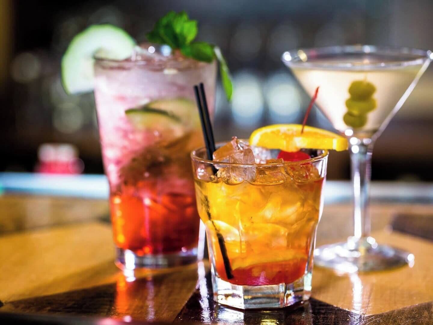 Trois cocktails sur le comptoir en bois d’un bar.