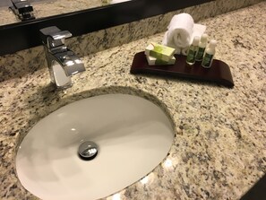 A bathroom sink with a granite countertop, a mirror, and toiletries on a tray.