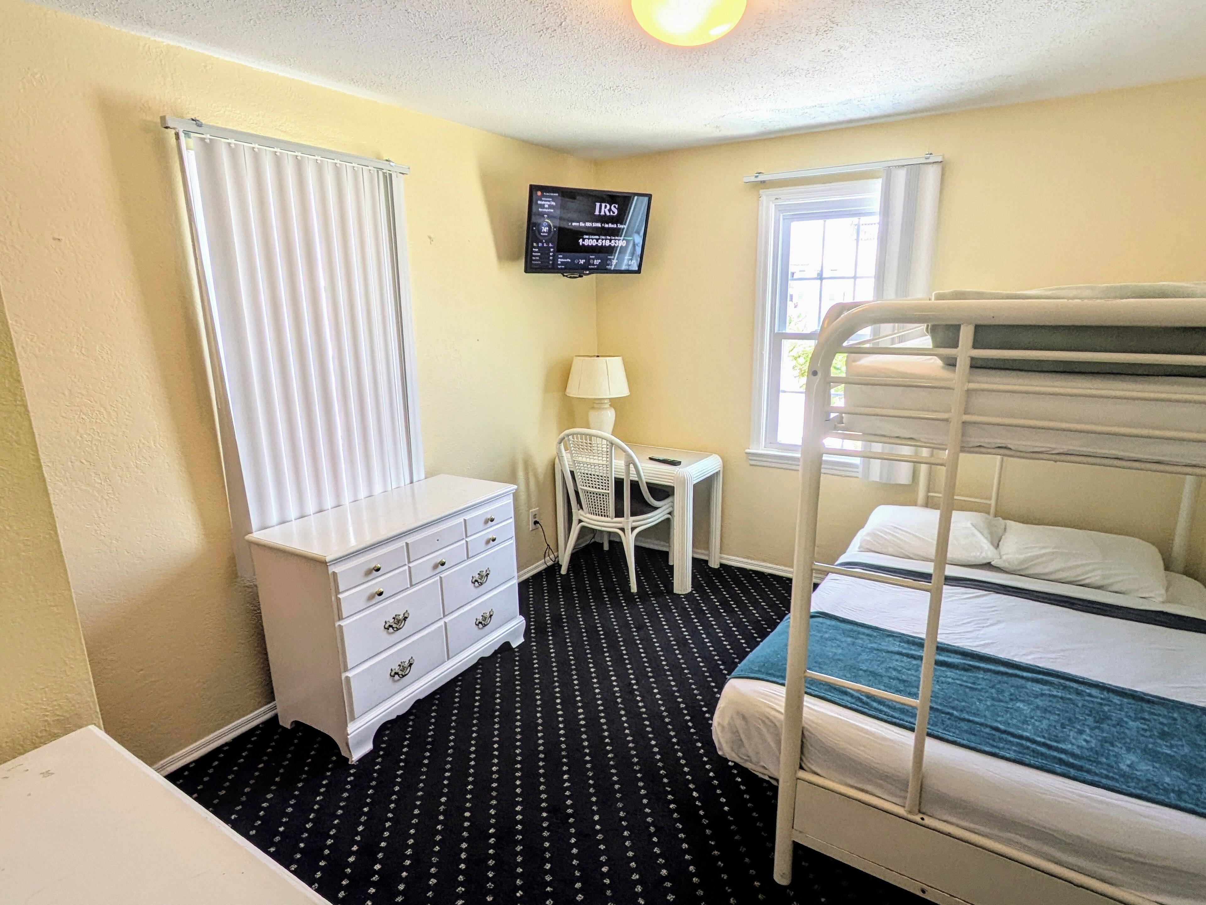 A small, compact room with a bunk bed, a desk with a chair, a dresser, and a TV mounted on the wall.