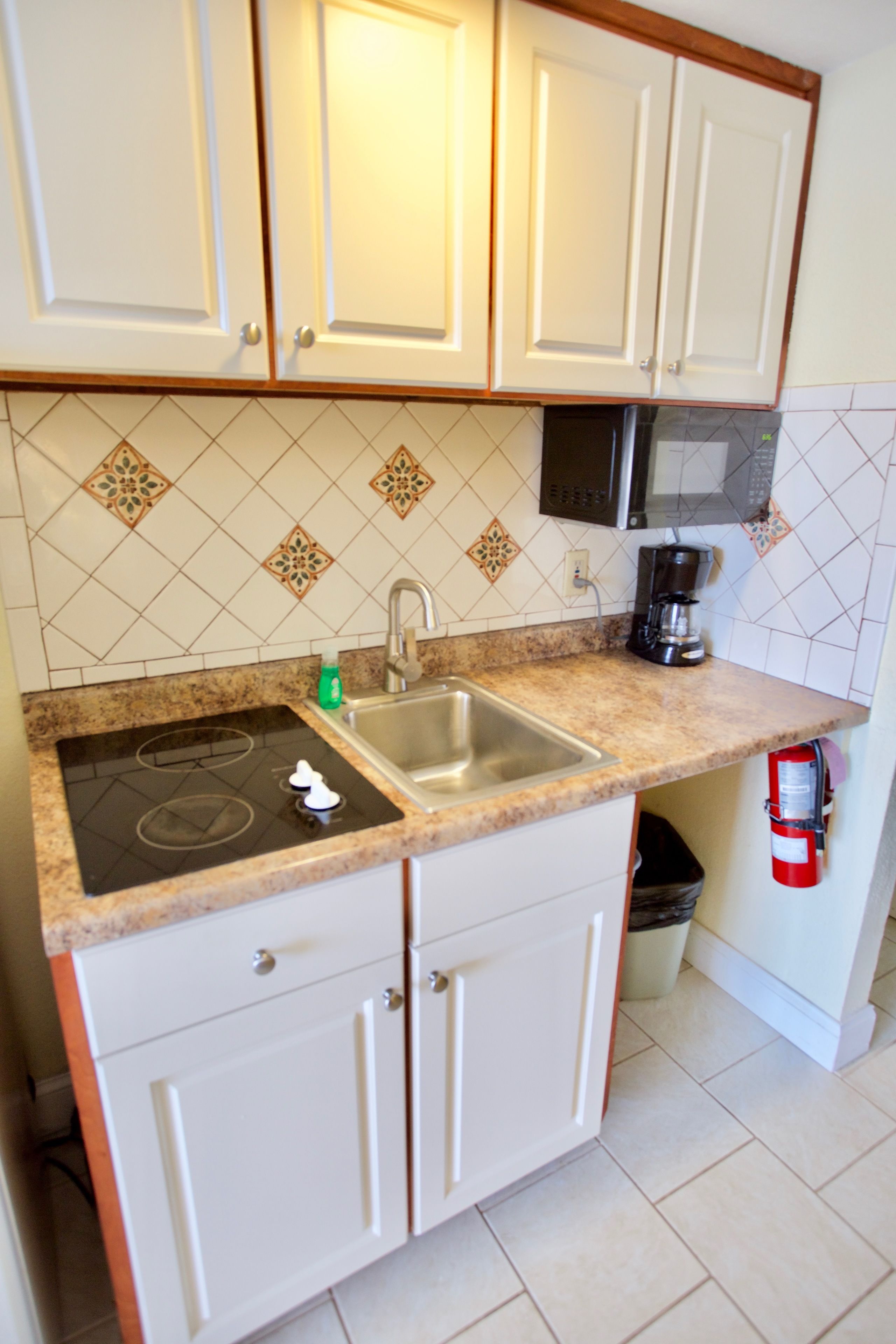 A kitchen with white cabinets, a stainless steel sink, a black stove, and a microwave.