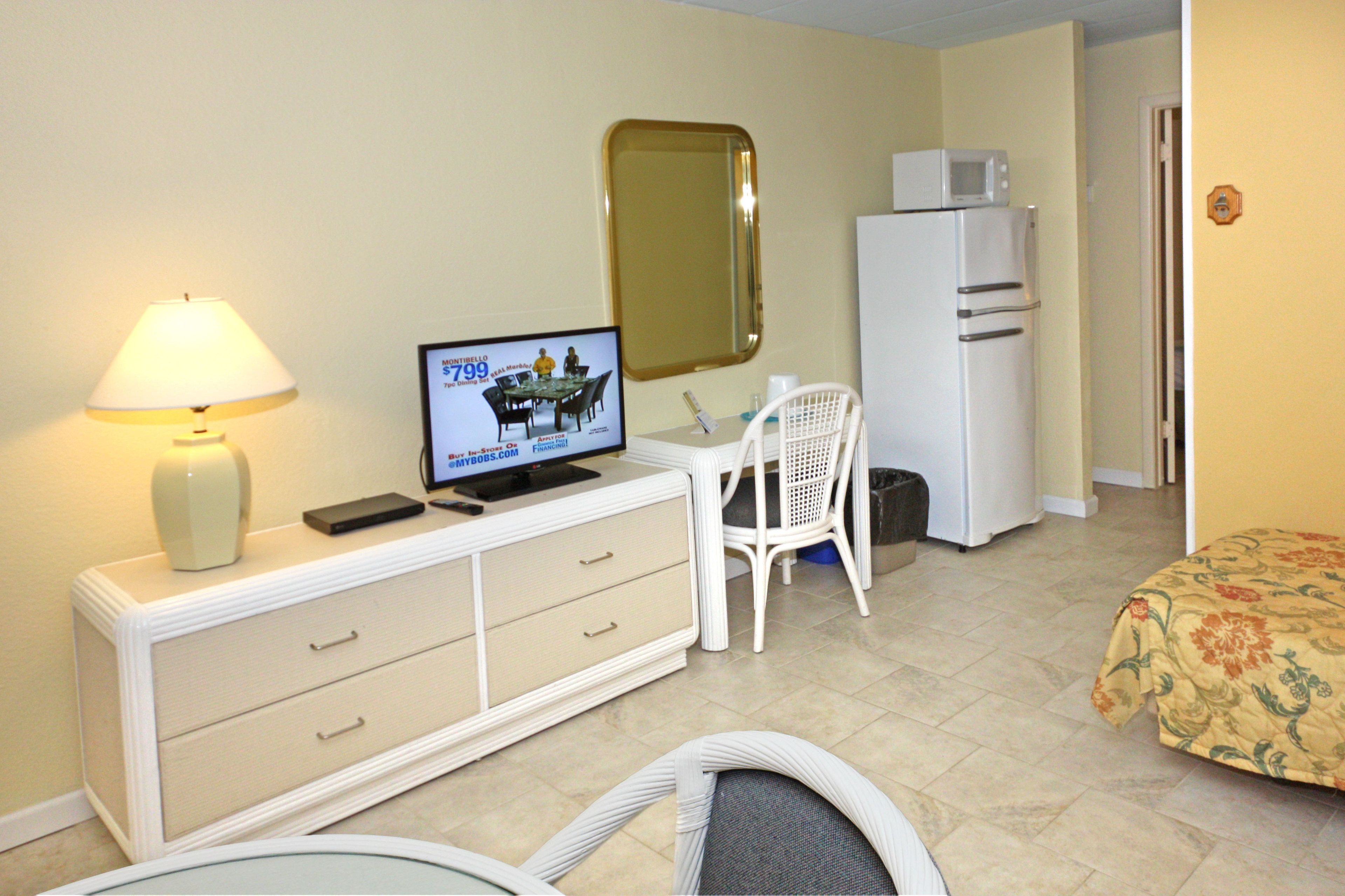 Habitación de hotel con televisión, escritorio, silla, cama, microondas y refrigerador.