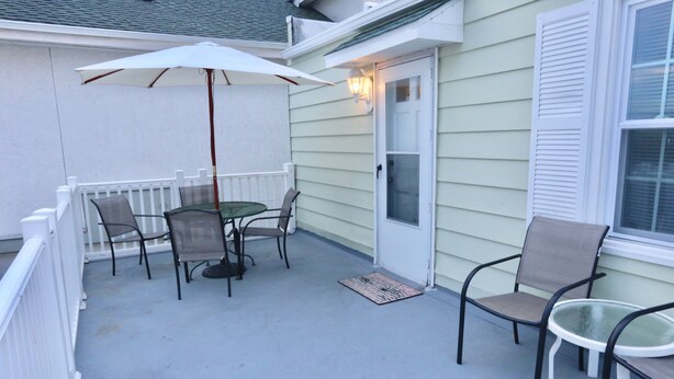A covered patio with a table and chairs, a white umbrella, and a door with a window. - Quebec Motel (Wildwood)