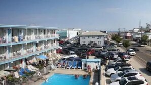 A hotel with a pool area, multiple balconies, and a parking lot. - Quebec Motel (Wildwood)