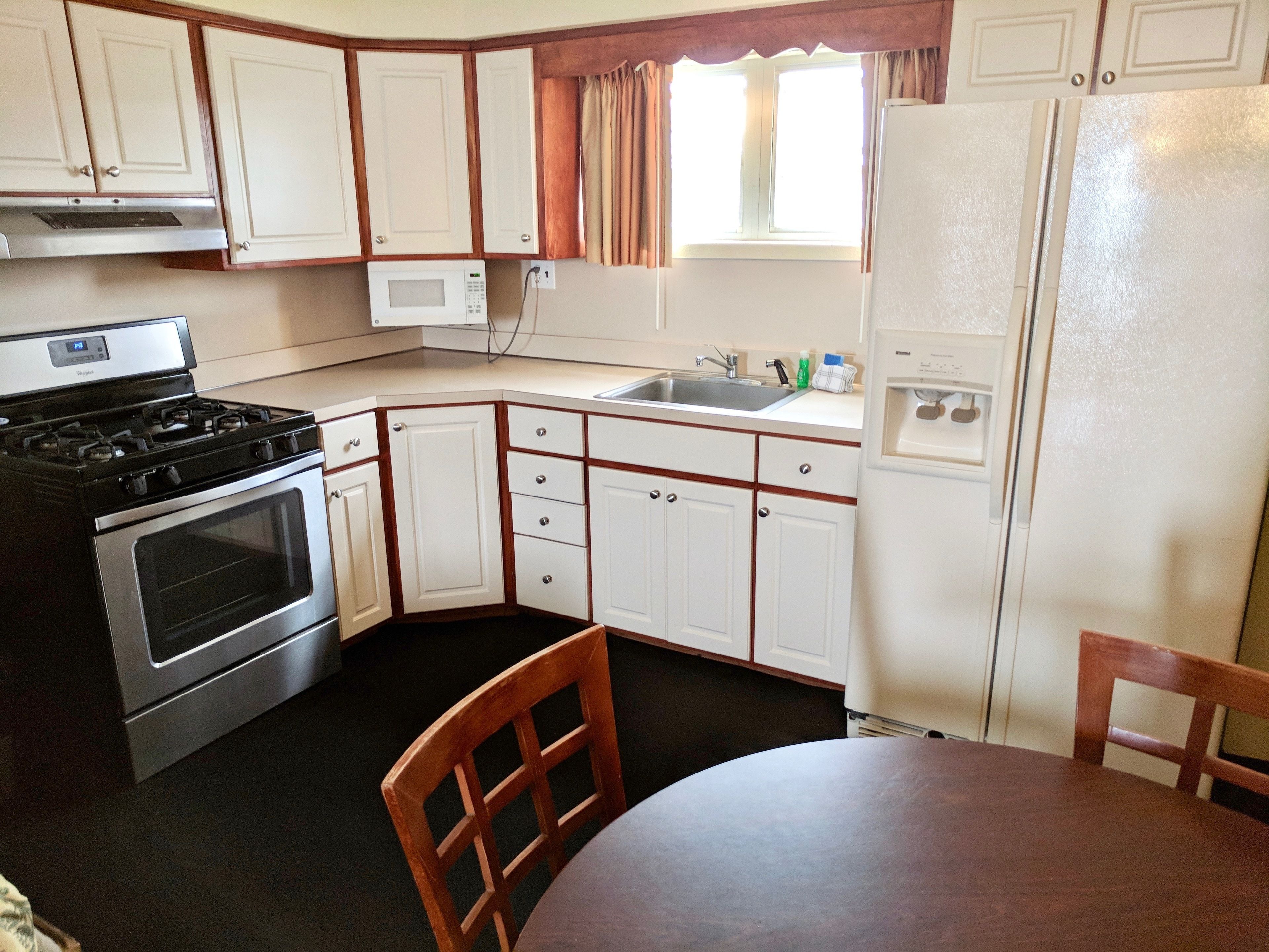 Una cocina compacta con armarios blancos, estufa, refrigerador y lavamanos.