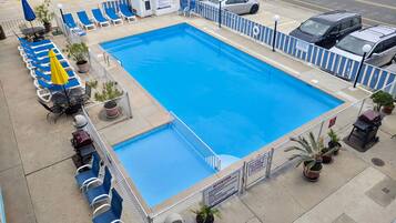 Una piscina rectangular con borde azul, rodeada de sillas reclinables azules y sombrillas amarillas.