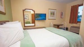 A hotel room with a large bed, a small table, a chair, a television, and a window with curtains.