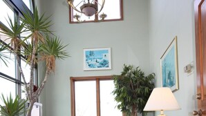 A living room with a large window, a chandelier, a green armchair, a gray sofa, a wooden side table with a lamp, and a patterned rug.