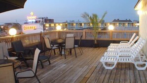 A wooden deck with outdoor seating, including chairs and a table, overlooking a cityscape with a visible 'Quebec' sign.