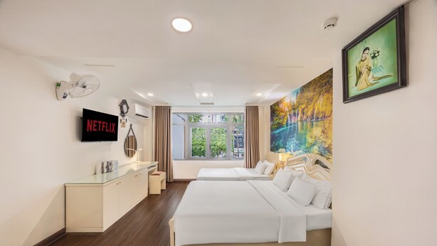 A hotel room with two beds, a TV, a painting, and a window with a view.