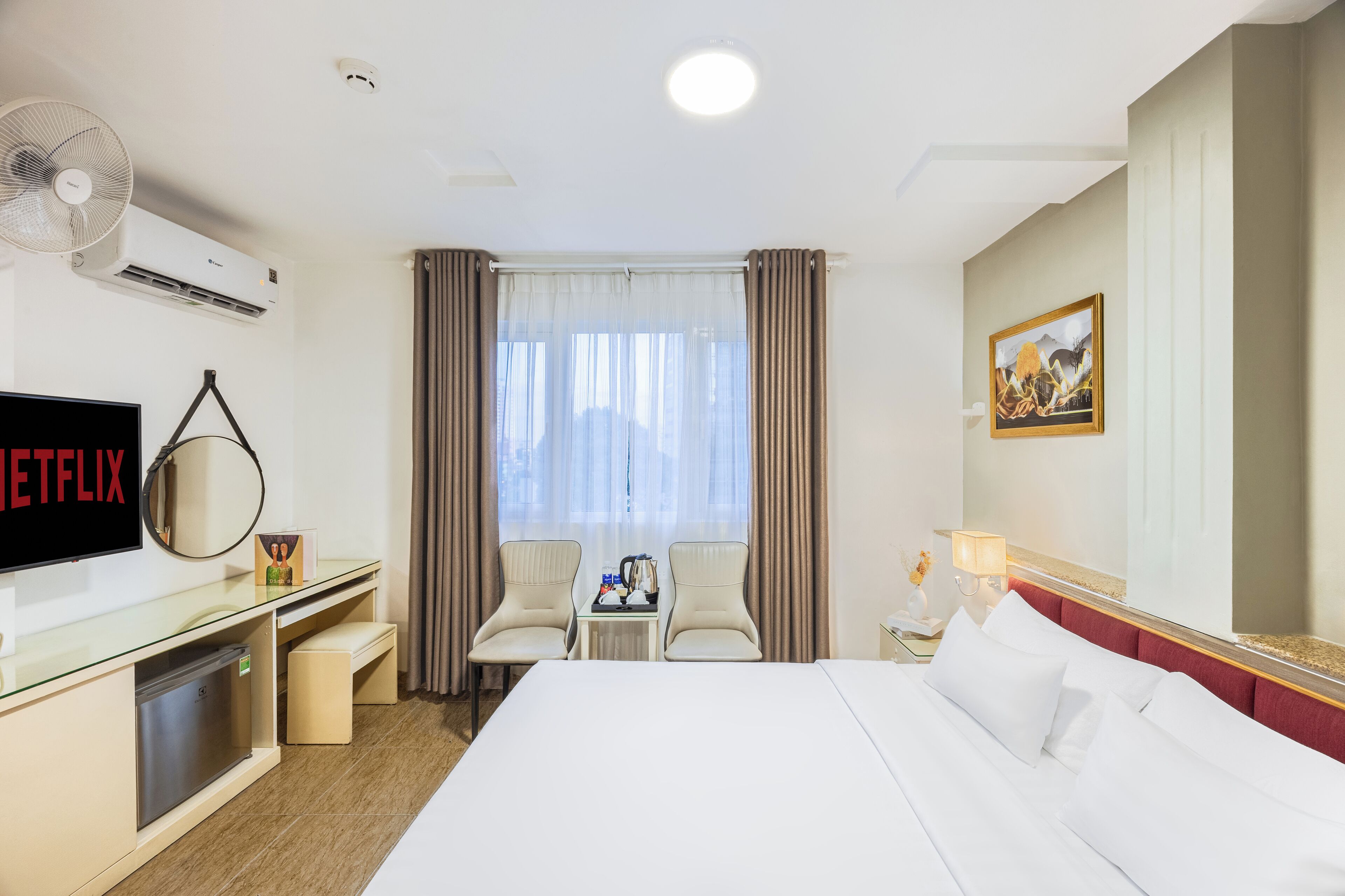 Une chambre d’hôtel avec un lit, un bureau avec un ordinateur, une télévision et une fenêtre avec des rideaux.