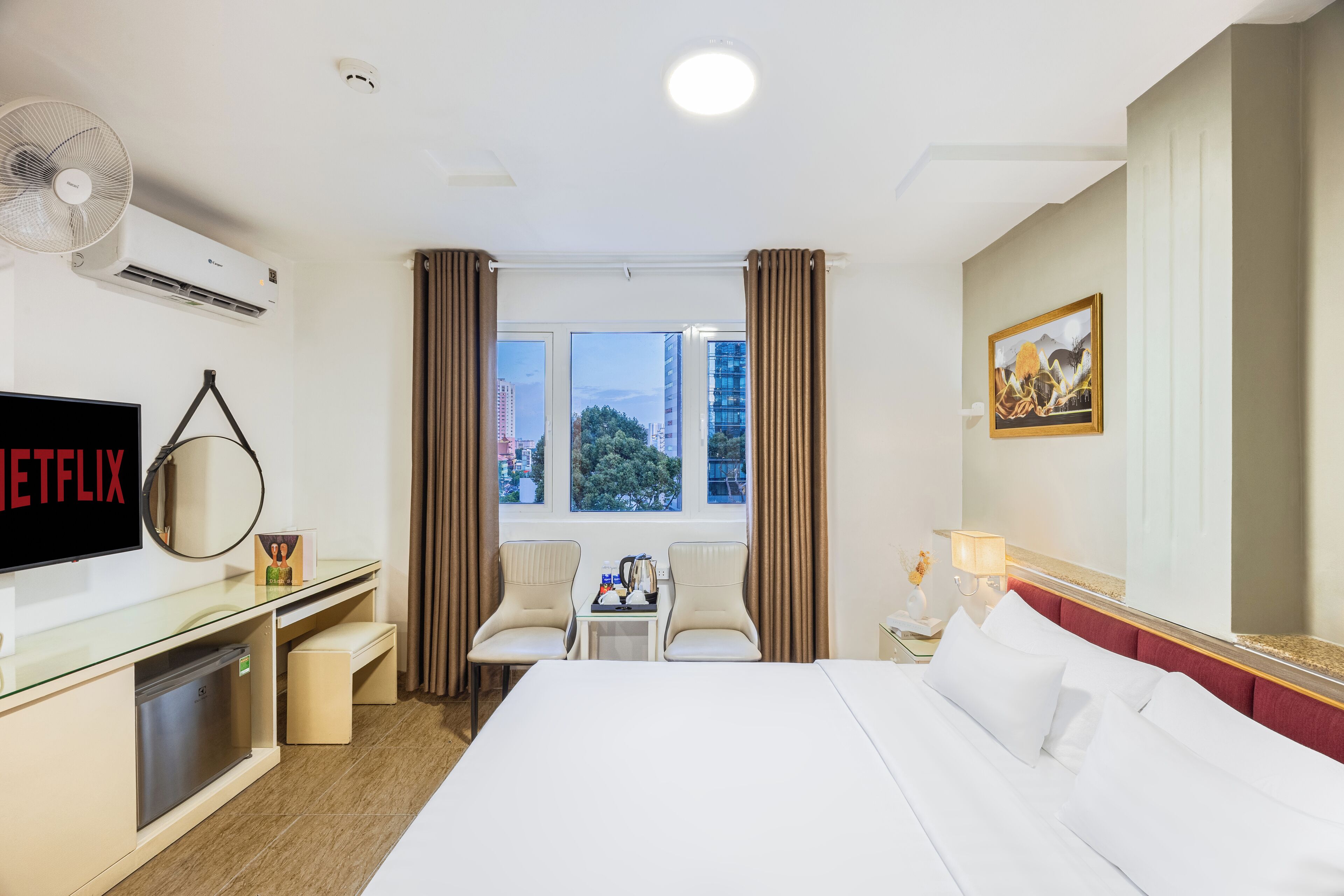 A hotel room with a bed, a desk with a computer, a TV, and a window with curtains.
